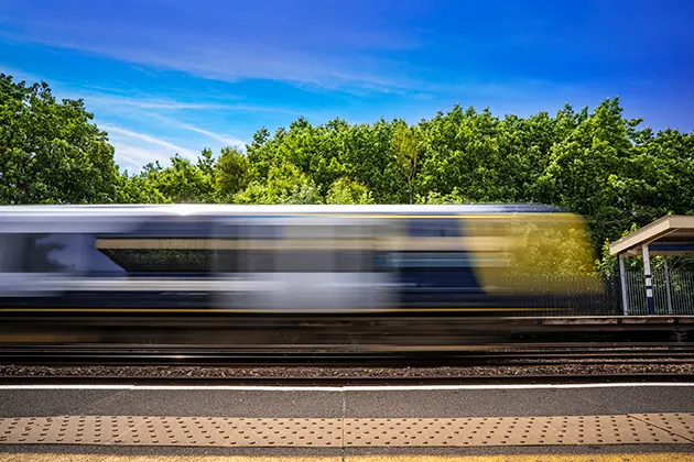 A blurred image of a train moving at speed along railway tracks on a sunny day.