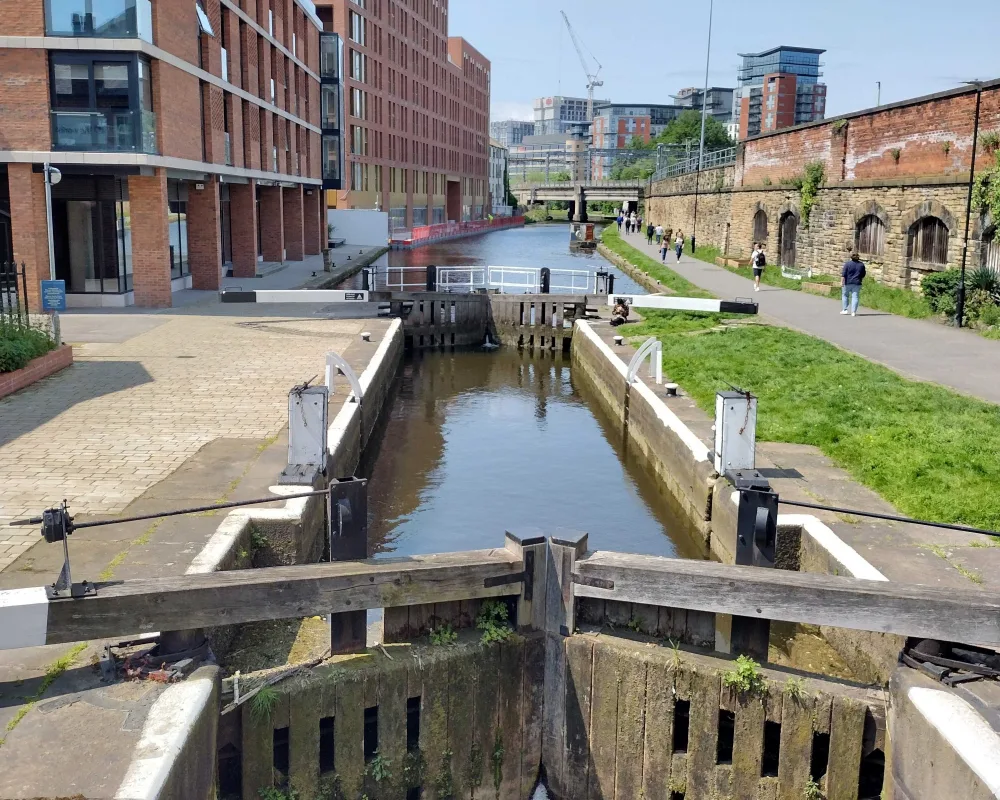 A city-centre canal with red brick buildings either side and wooden locks across the water. 