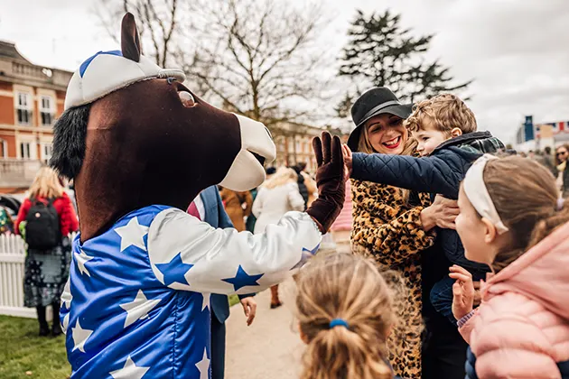 A person wearing a racehorse costume gives a high five to a young boy.
