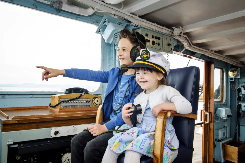 A young white boy and girl sitting in the captain's chair aboard a yacht.