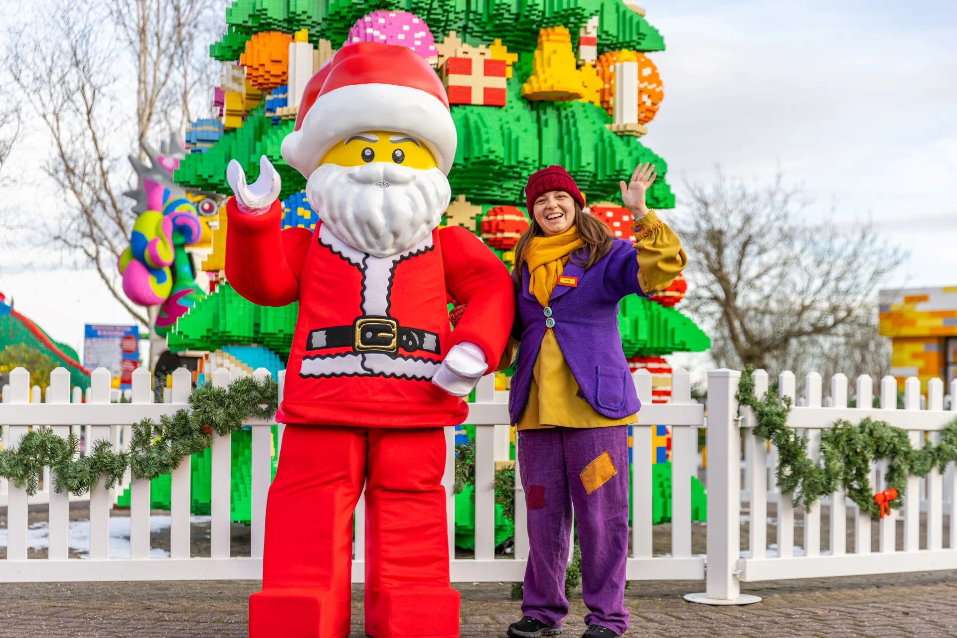 A LEGO Christmas tree with someone dressed in a LEGO Santa outfit and a white woman dressed as an elf standing in front. 
