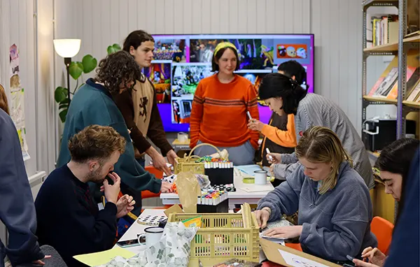 A group of young adults sitting and standing around a table loaded with craft supplies. 