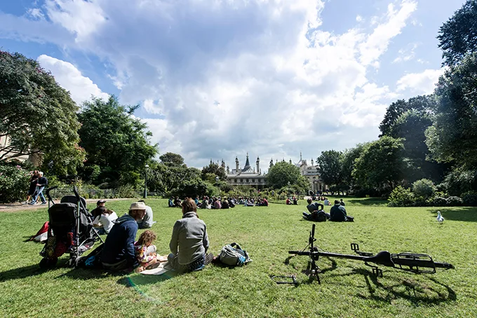 Groups of people sit on a lawn in front of the Royal Pavilion in Brighton on a sunny day. 