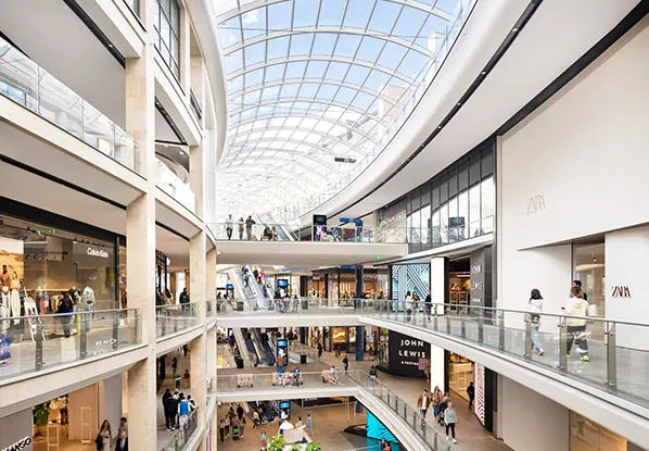 Inside a bright multilevel shopping centre with a large glass roof and clean white walls.