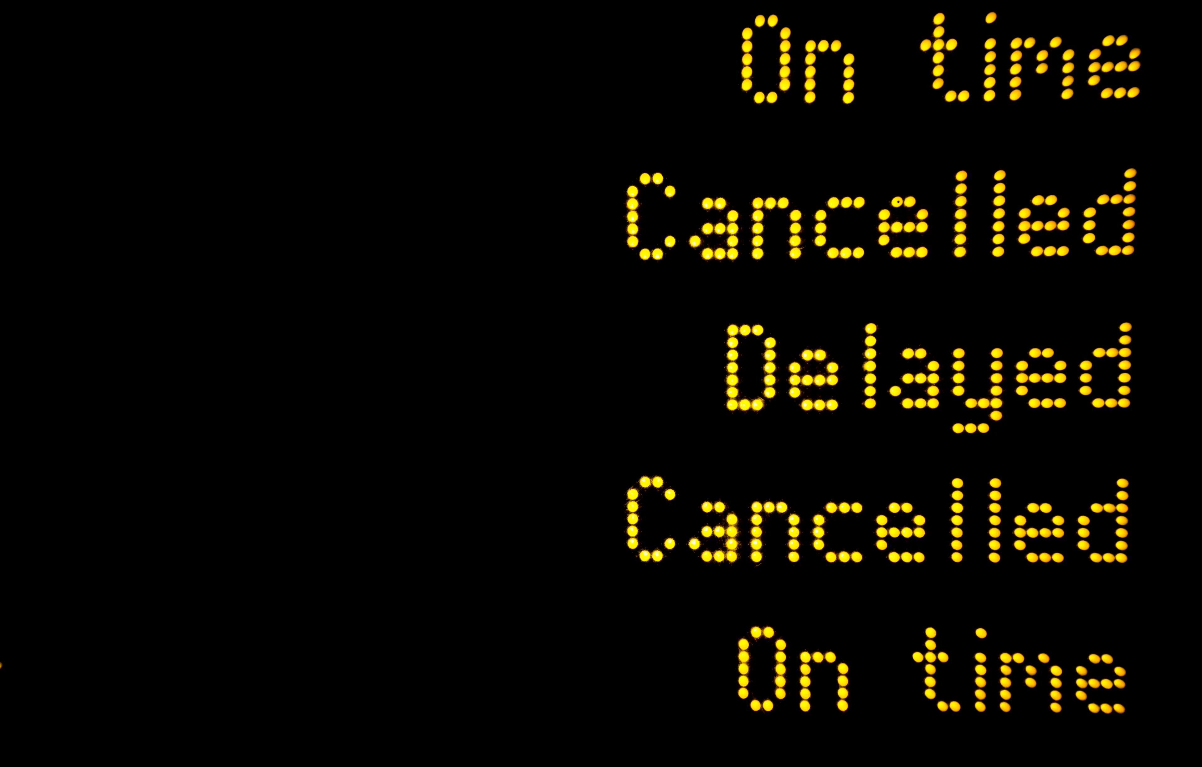 A black departure board with yellow digital text that reads: On time, Cancelled, Delayed, Cancelled, On time. 