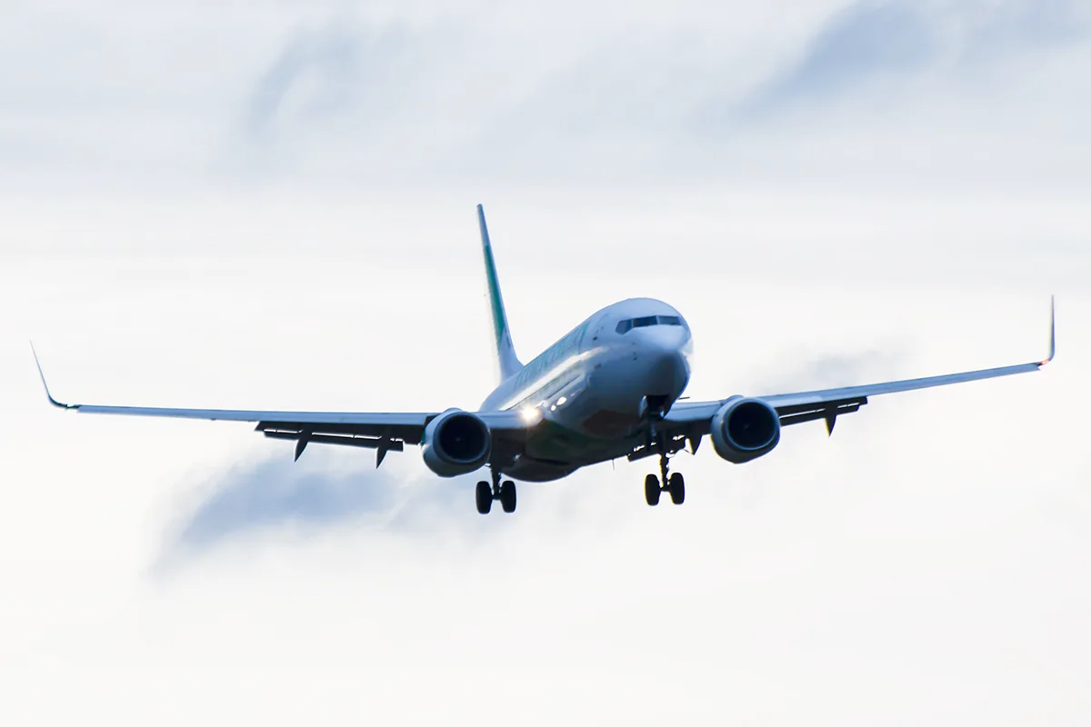 A silver grey passenger aircraft in flight against a grey white sky. 