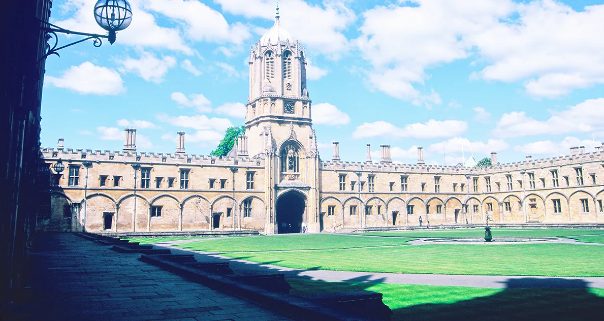 A historic Oxford university building with a tower looking over a grass lawn.