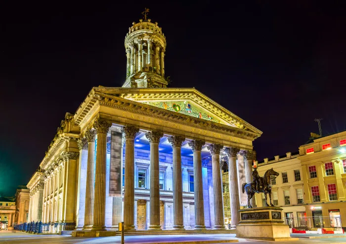 Gallery of modern art in Glasgow lit up at nighttime with Pillars at the front of the gallery standing out with blue lights behind.