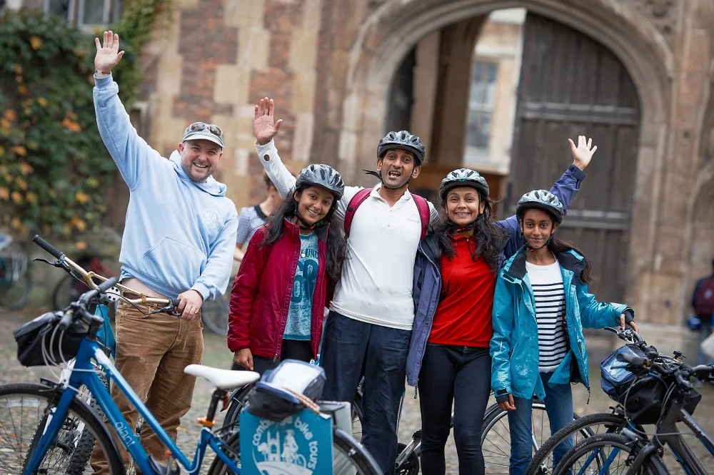 A white man in a baseball cap and an Asian family of 4 wearing bicycle helmets stand smiling next to bicycles