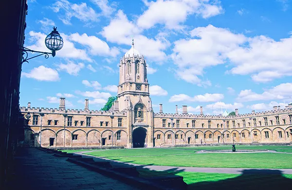 A historic Oxford university building with a tower looking over a grass lawn.