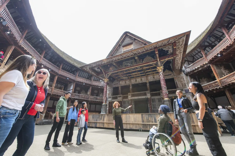 Visitors including a wheelchair user gather in the open-air courtyard of Shakespeare's Globe Theatre in London.