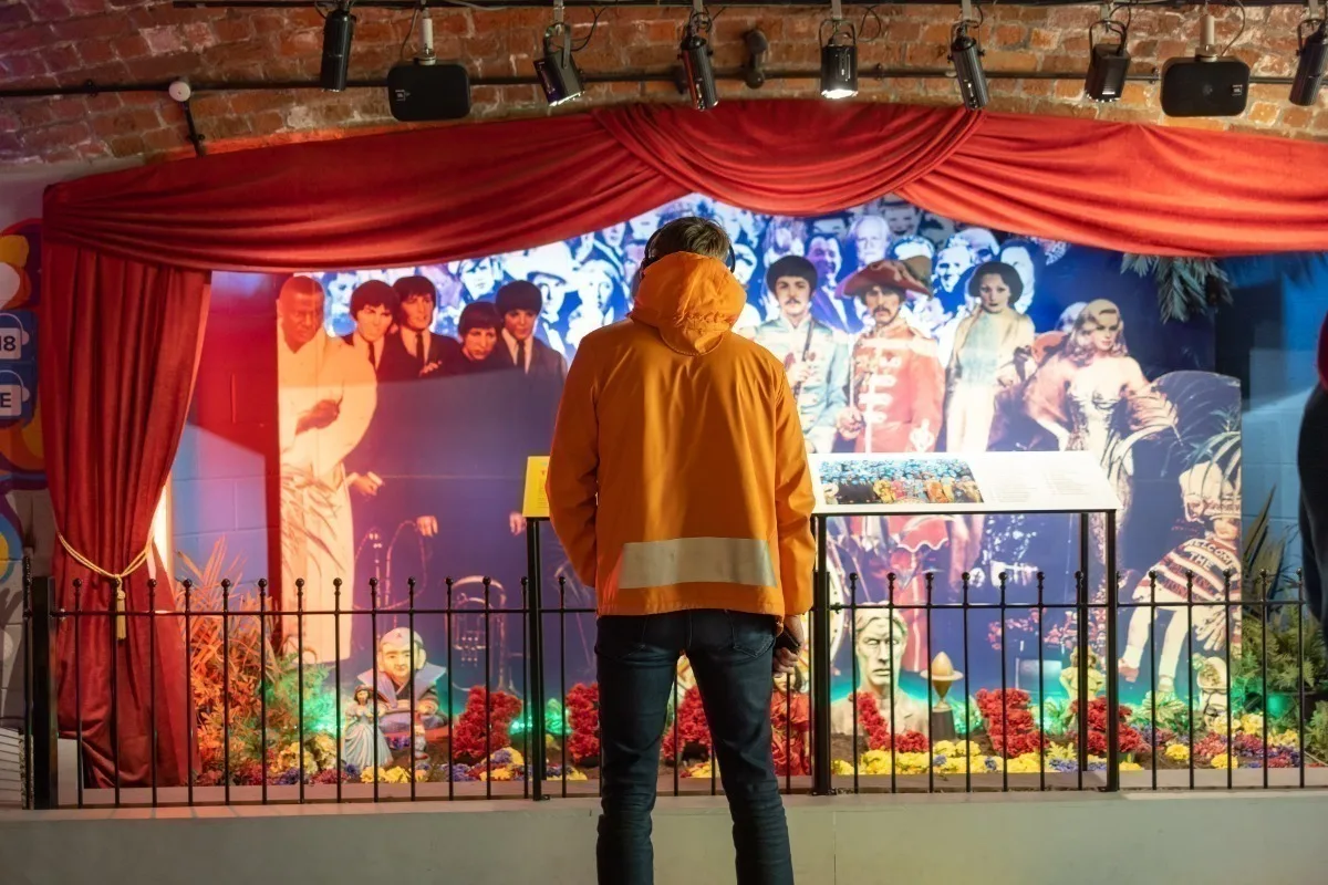 Rear view of a man in an orange waterproof jacket standing in front of a display of life-size images of The Beatles. 