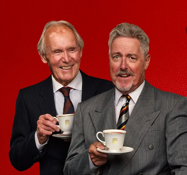 Actors Clive Francis and Griff Rhys Jones wearing suits and holding tea cups and saucers.