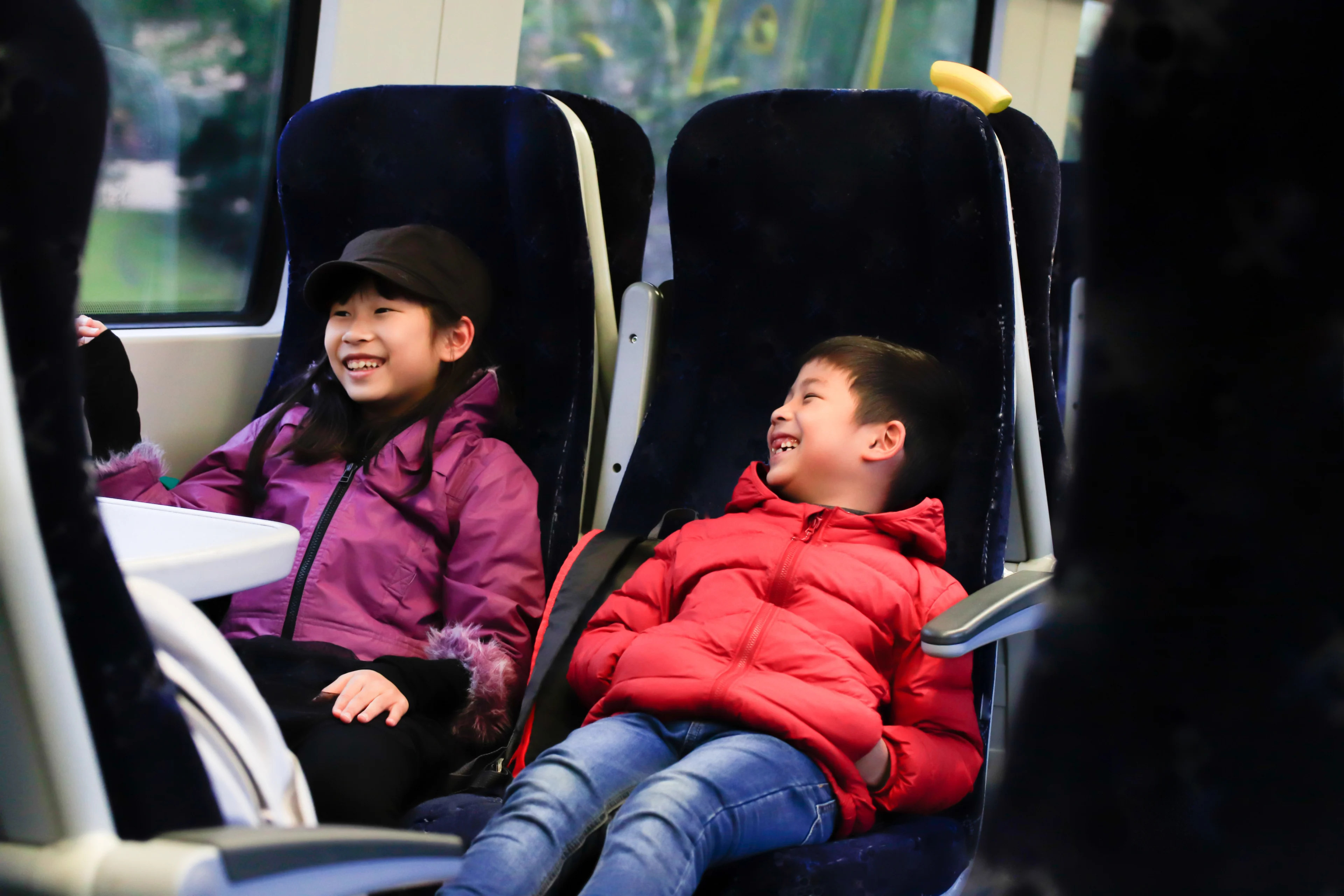 2 young children sitting on a train are laughing and smiling