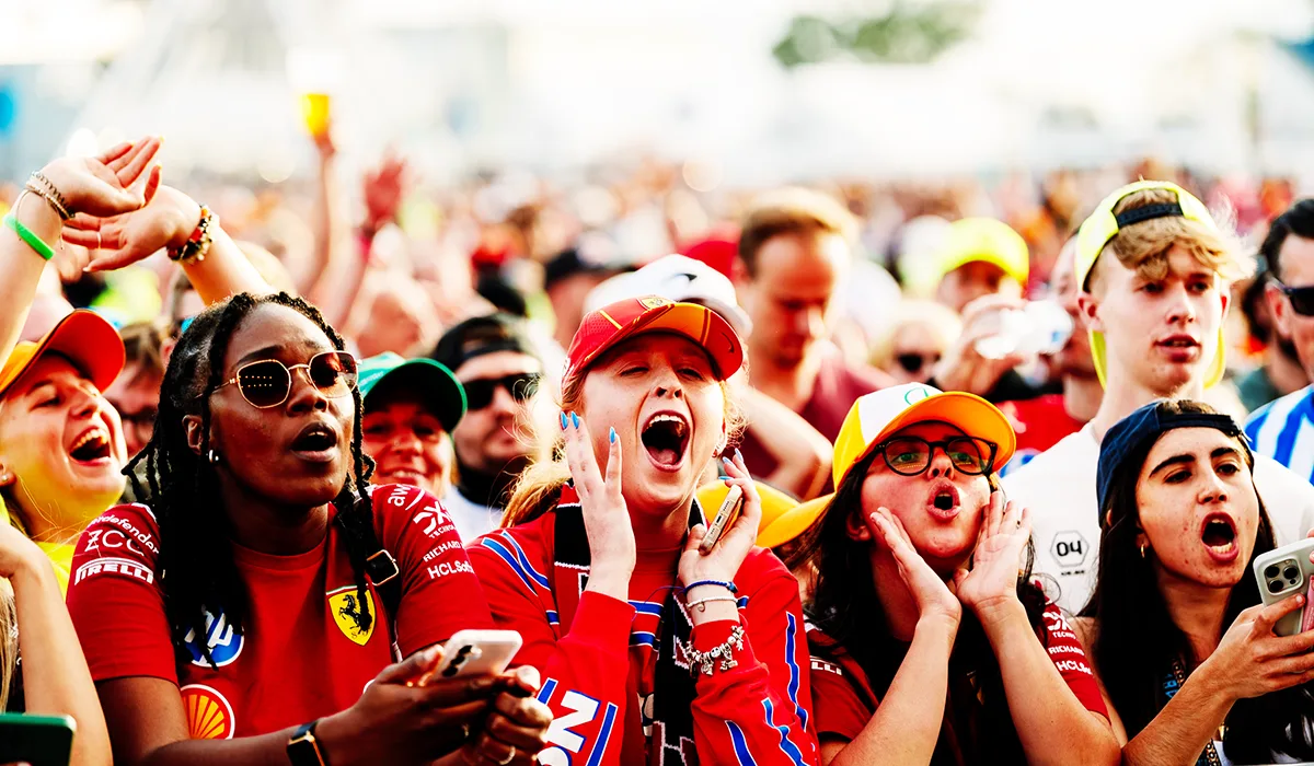 Excited crowd at a motorsport event, wearing colourful team merchandise and caps, cheering enthusiastically.