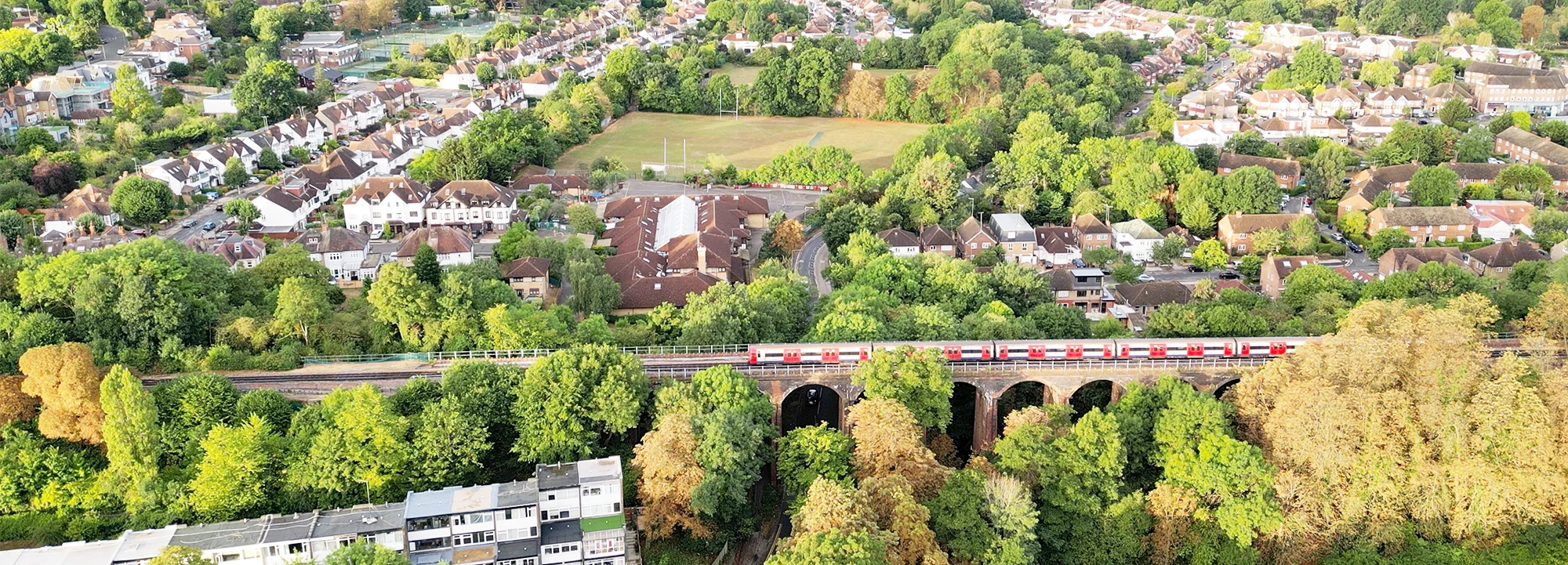 A train crosses a viaduct in a suburban area of north London in the daytime