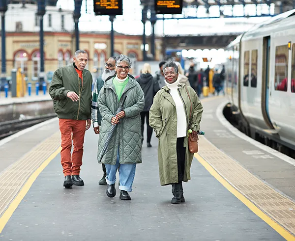 2 older Black men and 2 older Black women standing smiling on a station platform next to a train. 
