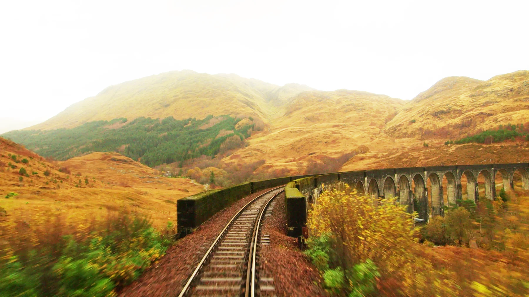 A train driver's eye view of a railway track crossing a viaduct with the Scottish highlands in autumn behind.