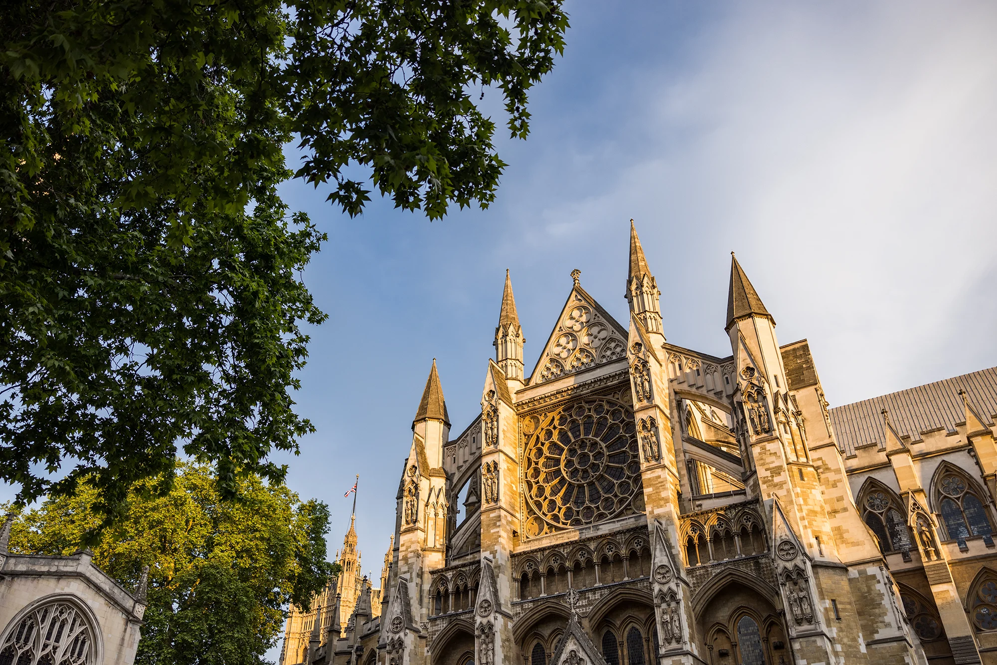 Looking up at the front of Westminster Abbey, with a blue sky above and a tree on the left