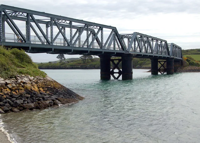 A grey metal railway bridge going over an estuary.