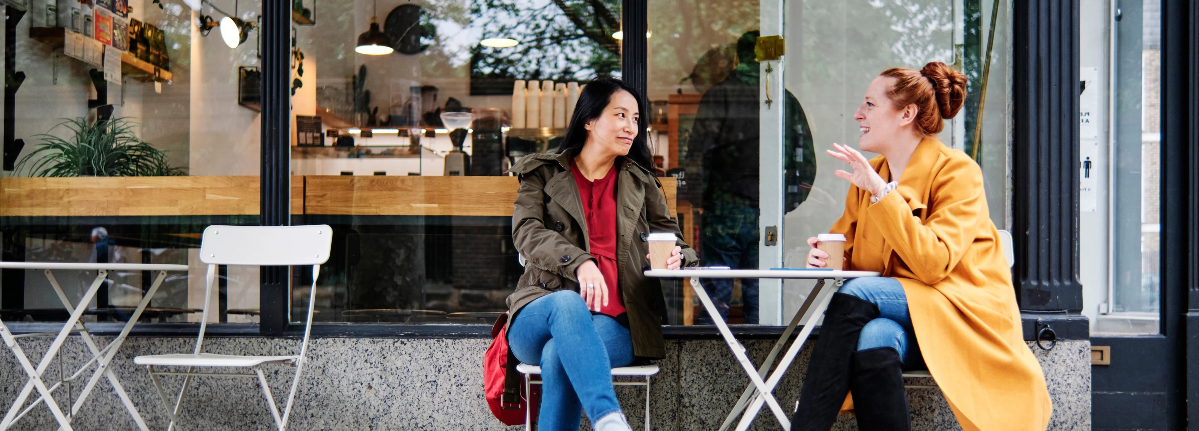 Two female friends drinking coffee at a table outside a coffee shop