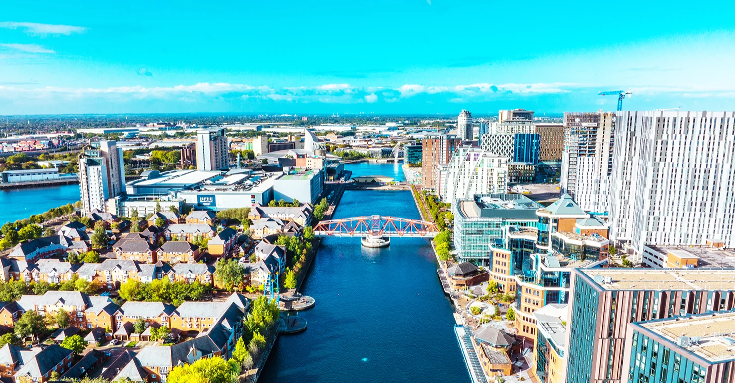 Aerial view of Manchester's Salford quays, with a large canal in the centre with bridges across, and tall buildings either side. 