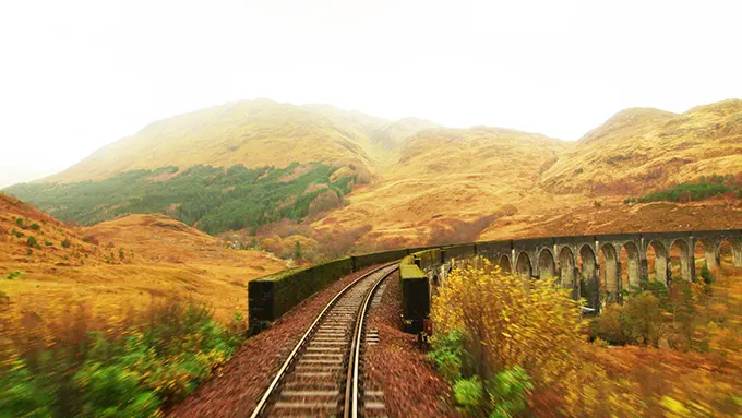 A train driver's eye view of a railway track crossing a viaduct with the Scottish highlands in autumn behind.