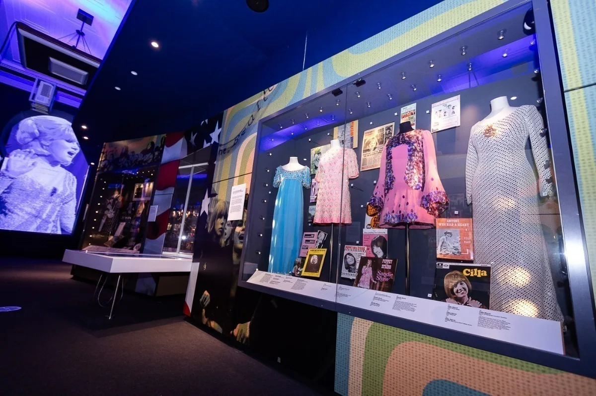 Museum display of vintage dresses and memorabilia from the 1960s music scene.