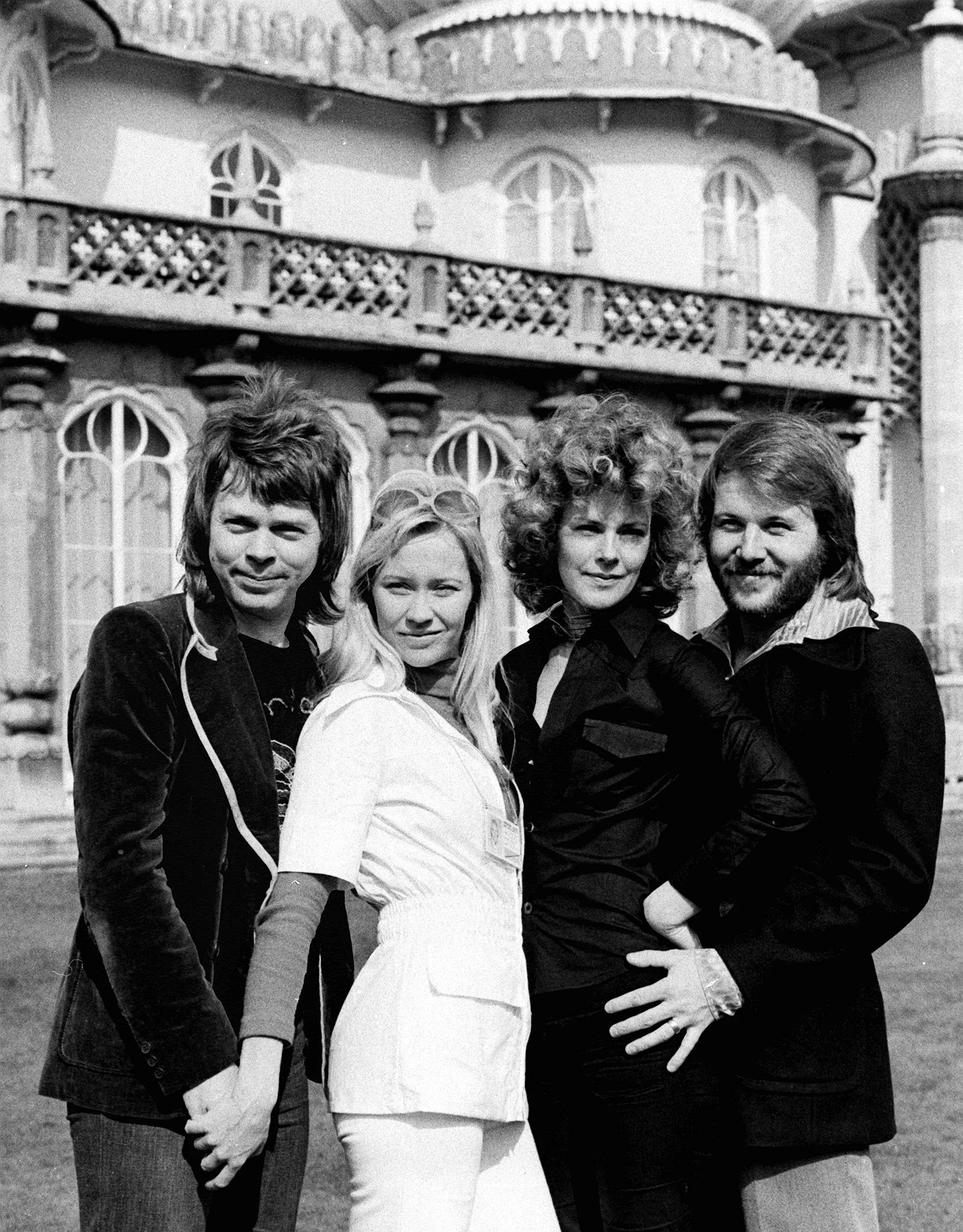 Black and white image of the group ABBA - 2 white men and 2 white women – standing on lawn in front of a large building. 