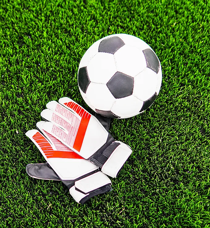 A football and a pair of goalkeeper's gloves on green grass
