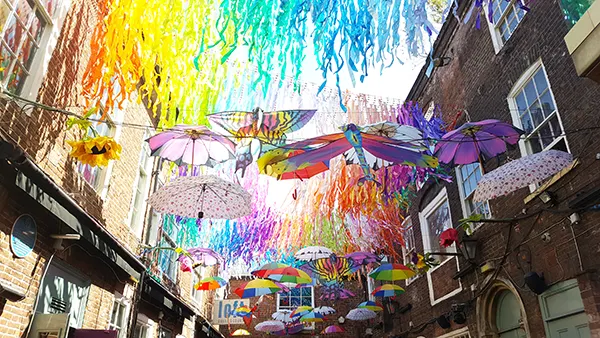 Colourful rainbow bunting, umbrellas and kites hanging between buildings to celebrate LGBTQIA+ Pride.