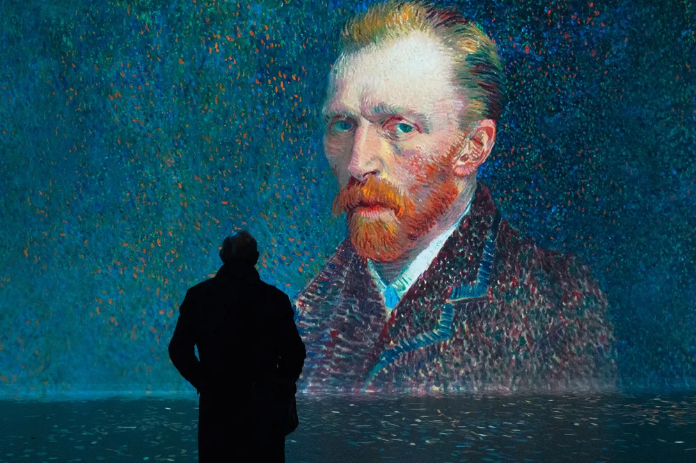 A silhouette of a man standing in front of a huge digital projection of a self portrait of the artist Vincent Van Gogh.