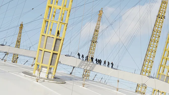 A group of people roped together and walking in a line on the roof of the O2 building. 