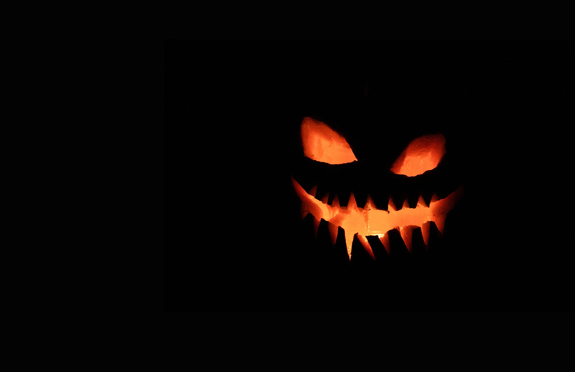 A spooky grinning pumpkin face glowing orange against a black background
