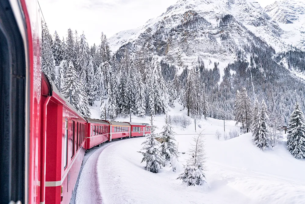 A red Swiss train goes through a snowy mountain pass.