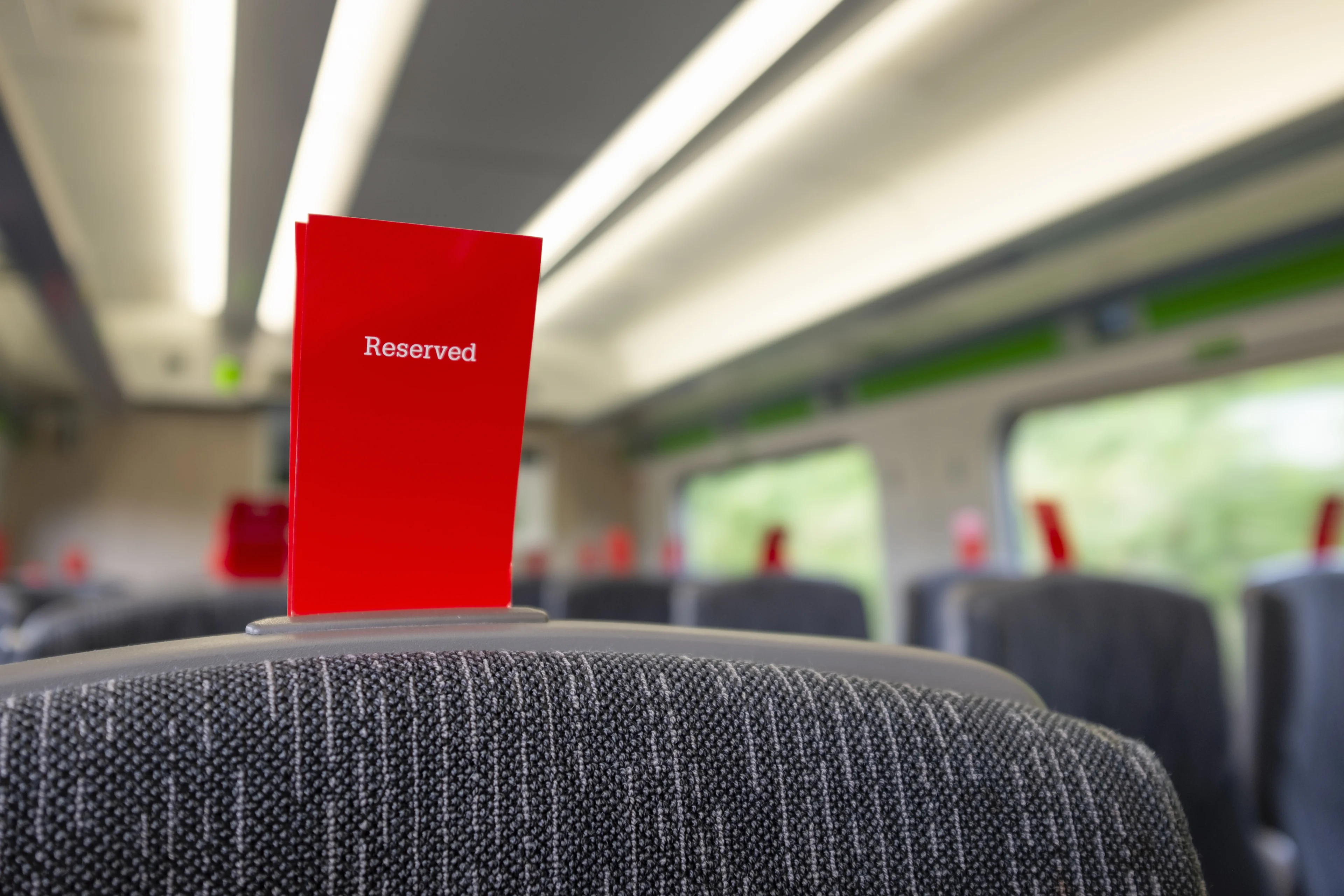 A red 'Reserved' ticket sitting in the slot on the top of a seat on a train