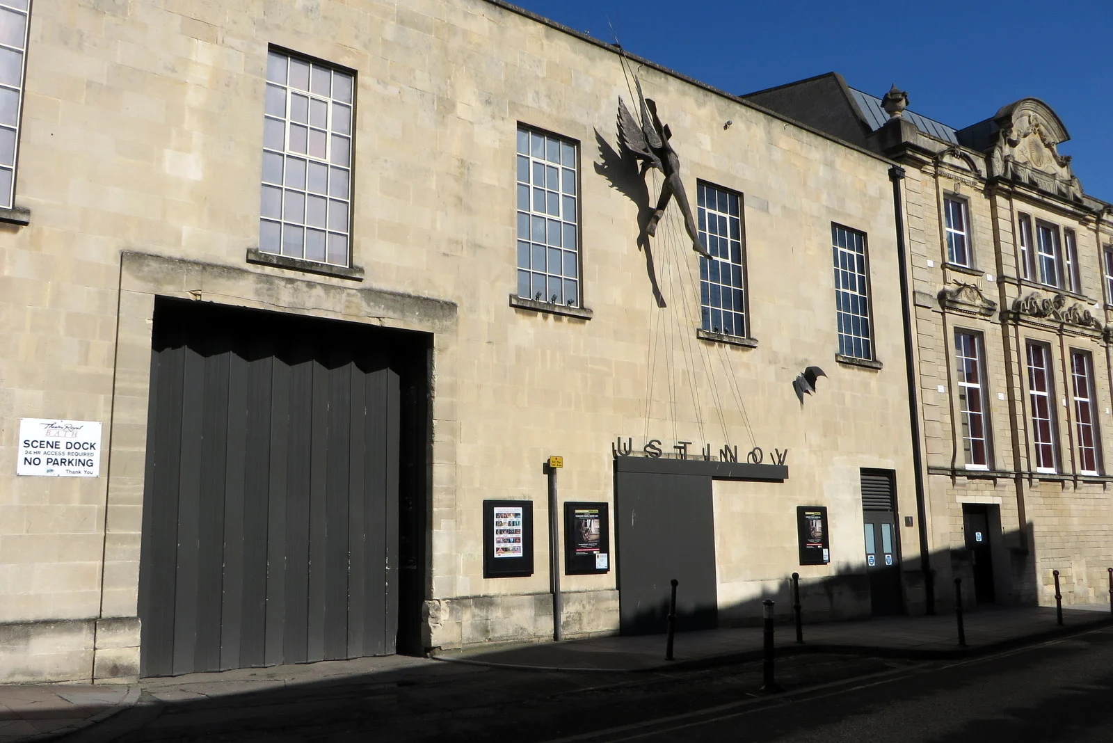 A 2-storey sandstone building with a large bronze statue of a winged figure attached to the wall. 