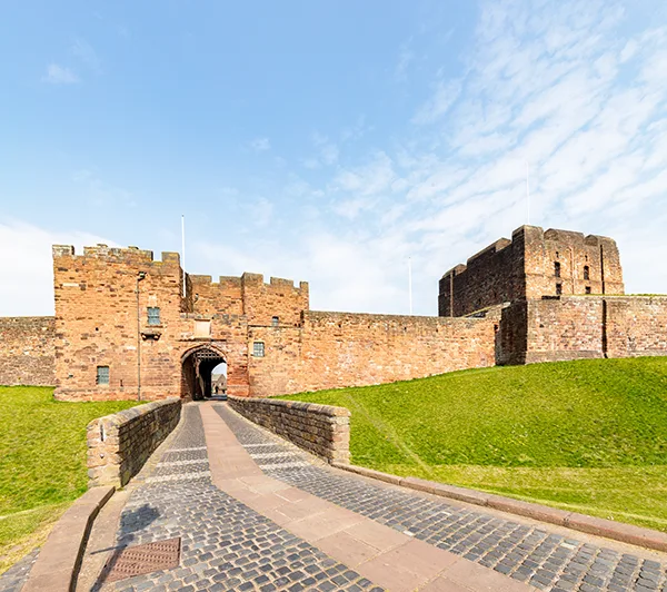 A brick path leading up to an ancient stone castle, with square towers and turrets. 