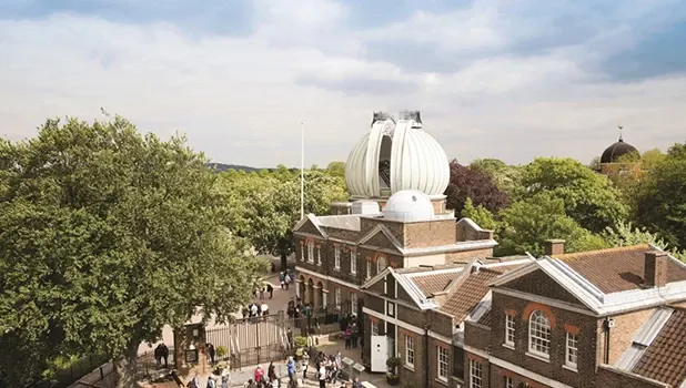 Royal Observatory Greenwich with distinctive white dome surrounded by trees and historic buildings under cloudy sky.