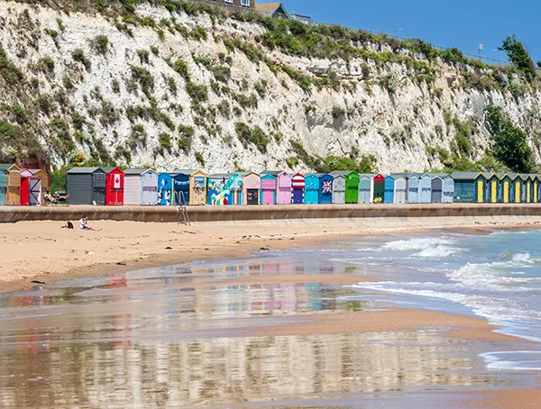 A row of colourful beach huts in Broadstairs, Kent, with the sea in the foreground and cliffs behind.