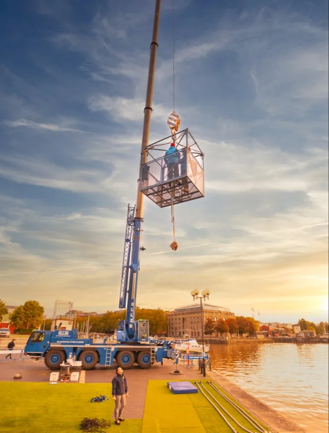 A person standing in a cage hanging from a crane, preparing to do a bungee jump. 