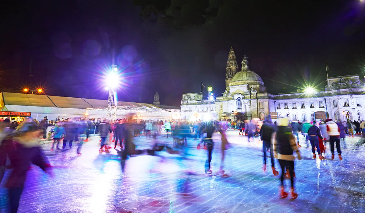 Ice skaters on an open-air city centre rink at night.