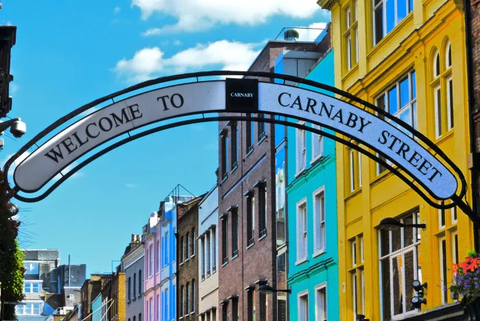Welcome to Carnaby street sign overlooking Carnaby Street in central London with a terrace of high buildings in multiple colours.