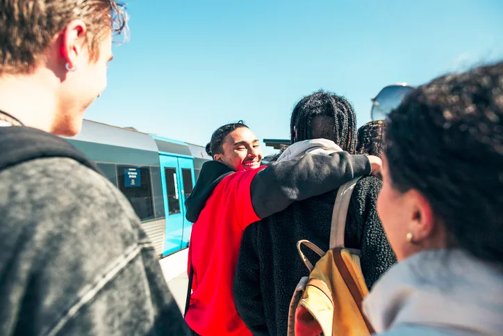 A multi-racial group of young people on a train platform. 