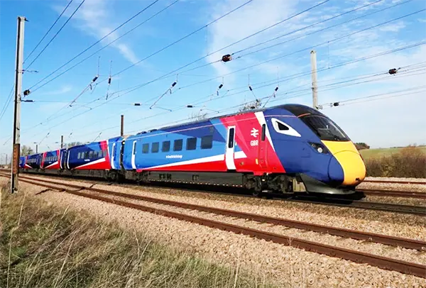 Train with blue, red and yellow livery and Great British Railways logo travelling through countryside under clear blue sky.