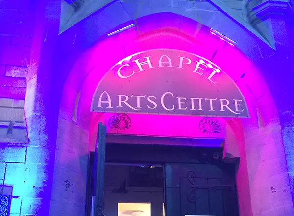 A neon-pink light above an arched doorway, illuminating a sign that reads CHAPEL ARTS CENTRE