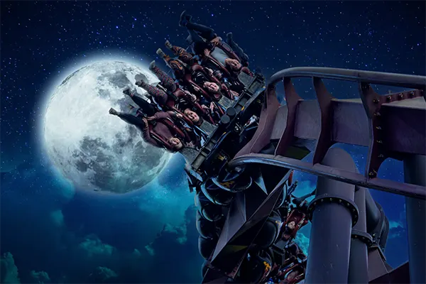 Riders on a theme park ride flipping upside down against a dark night sky and oversized full moon. 