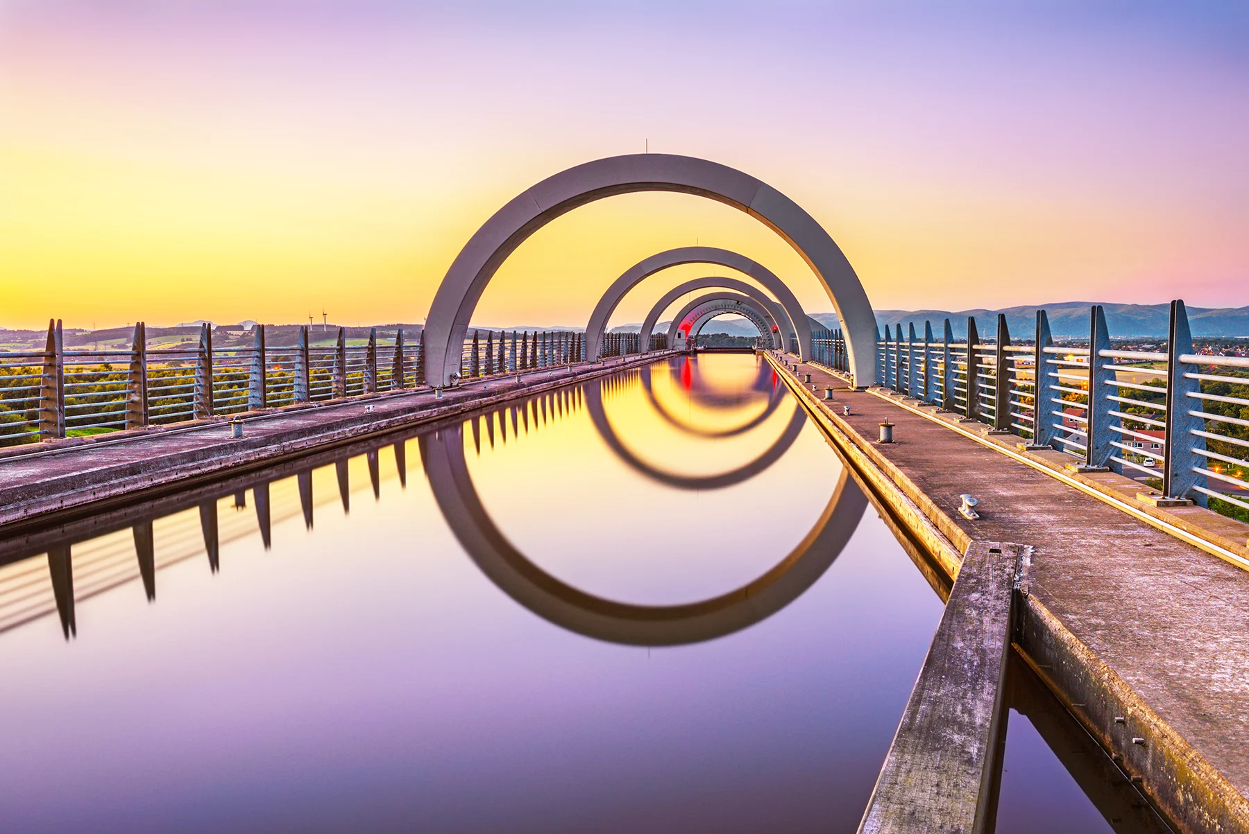A water-filled concrete walkway with semi circular arches reflected in the water, at dusk. 