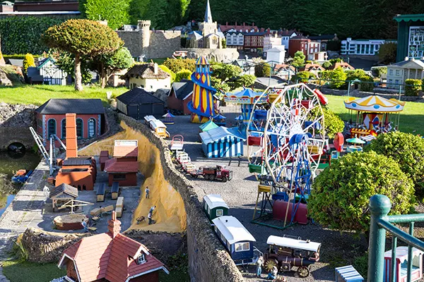 A detailed miniature model village featuring a fairground with a Ferris wheel, carousel, and colourful tents, surrounded by tiny buildings.