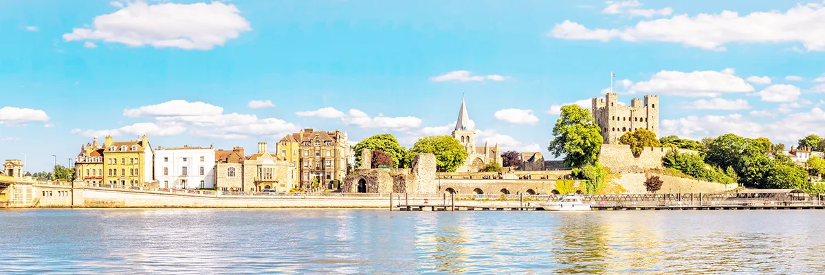 View from the river in Rochester, Kent, looking at a historic castle and cathedral alongside other buildings. 